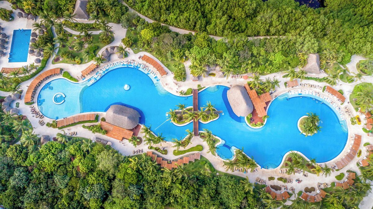 Surrounded by lush greenery and palm trees, this resort offers a serene environment with multiple interconnected pools and a central water feature.