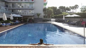 Una piscina al aire libre de temporada, sombrillas, tumbonas