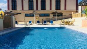 Una piscina al aire libre de temporada, sombrillas, tumbonas