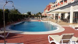 Una piscina al aire libre de temporada, sombrillas, tumbonas