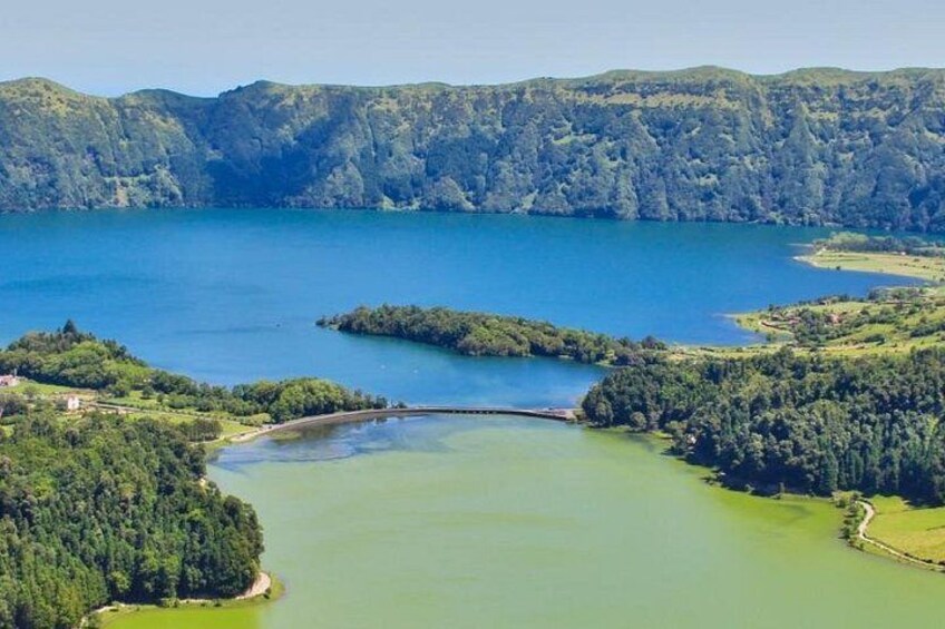 Un lago rodeado de colinas boscosas, una pequeña isla y un puente. 4