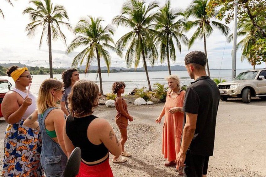 A group of people standing on a beach with palm trees and a car in the background. 2