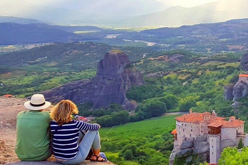A couple sitting on a cliff overlooking a valley with a castle-like structure. 1