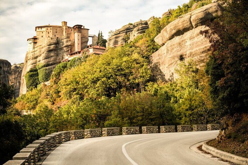 A winding road with a stone wall on one side and a castle on a rocky hill. 2