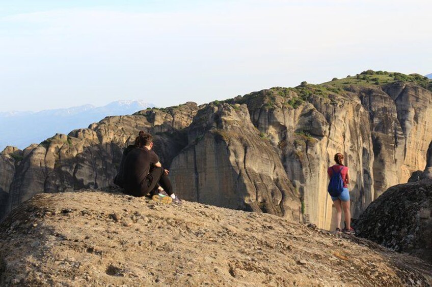 Dos personas sentadas y de pie en una colina rocosa, con montañas al fondo. 2