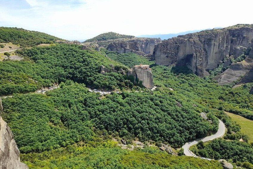 Un paisaje montañoso con densos bosques verdes, un camino serpenteante y una formación rocosa destacada. 4