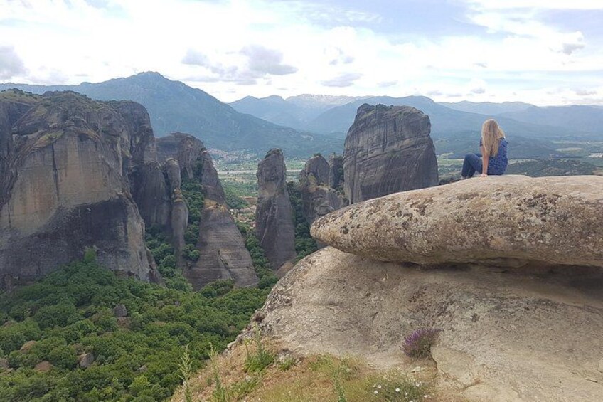 Una persona sentada sobre una roca contemplando un paisaje con formaciones rocosas singulares y montañas a lo lejos. 1