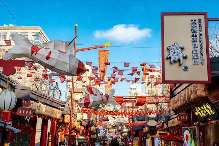 A street with red and white decorations, including large fish-shaped ornaments and red flags. 4