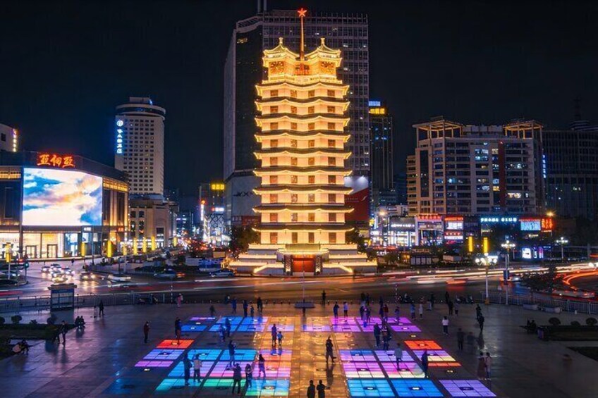 A brightly lit pagoda in the center of a city square with colorful lights on the ground. 2