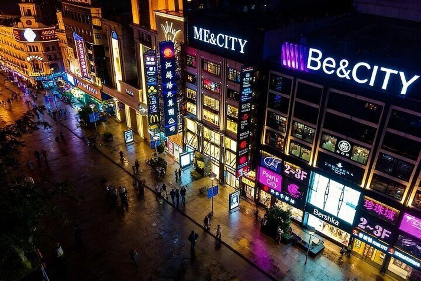 A brightly lit urban street at night with illuminated storefronts and signage, including 'ME&CITY' and 'Be&CITY'. 5