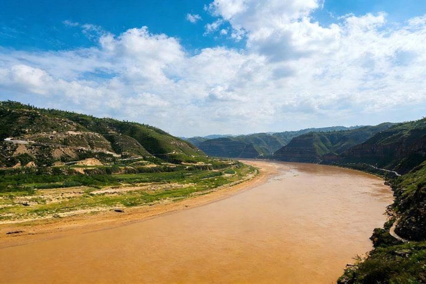 A wide river winding through a mountainous landscape with green hills on either side. 5