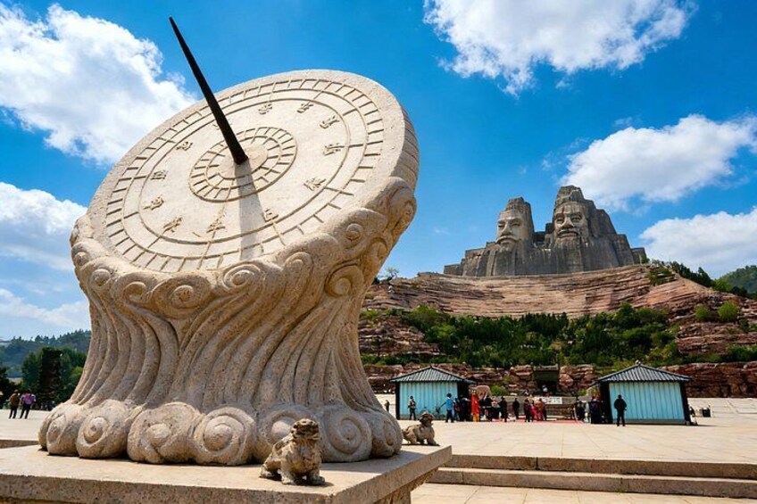 A large sundial with a clock face, a statue of a lion, and two large rock formations in the background. 4