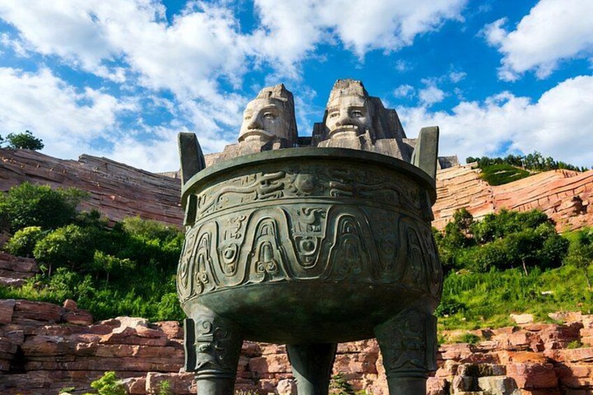 A large stone structure with intricate carvings, set against a backdrop of red rock formations and a clear blue sky. 3