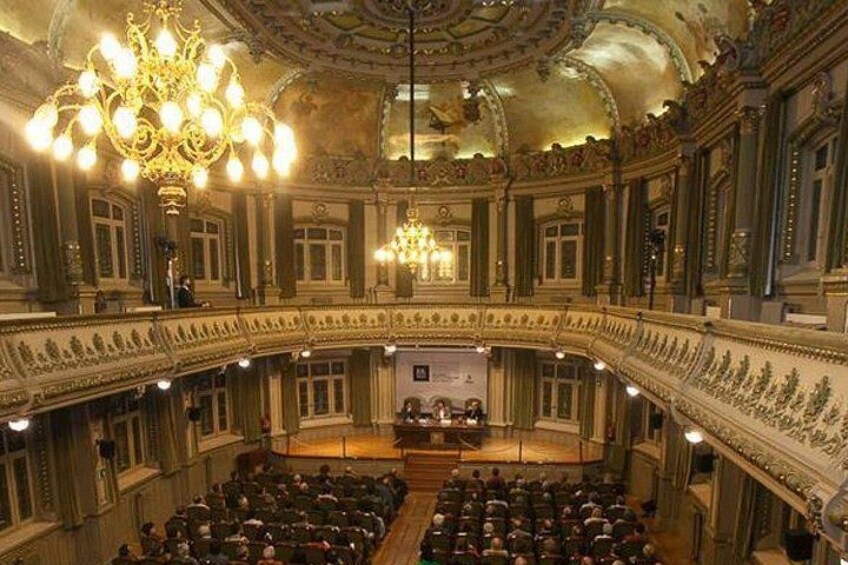 Un salón ricamente decorado con un escenario central, balcones y una araña. 3