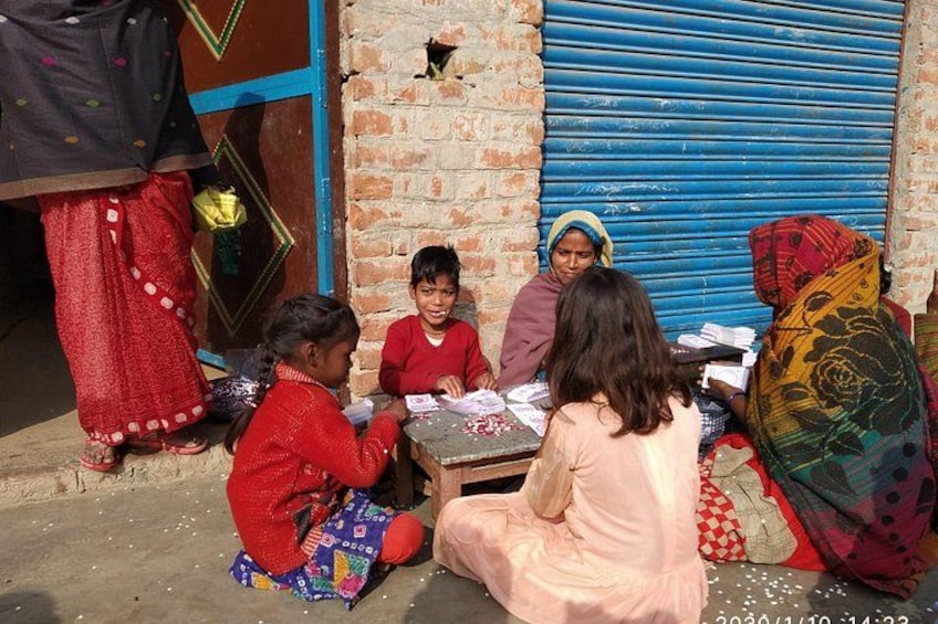 Children sitting on the ground in front of a brick wall with a blue shutter, engaged in an activity. 4