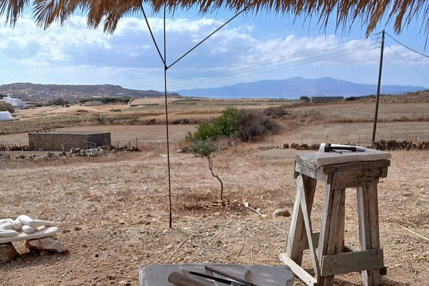 Un paysage aride et dégagé, avec un tabouret en bois, un petit arbre et des montagnes lointaines sous un ciel clair. 2