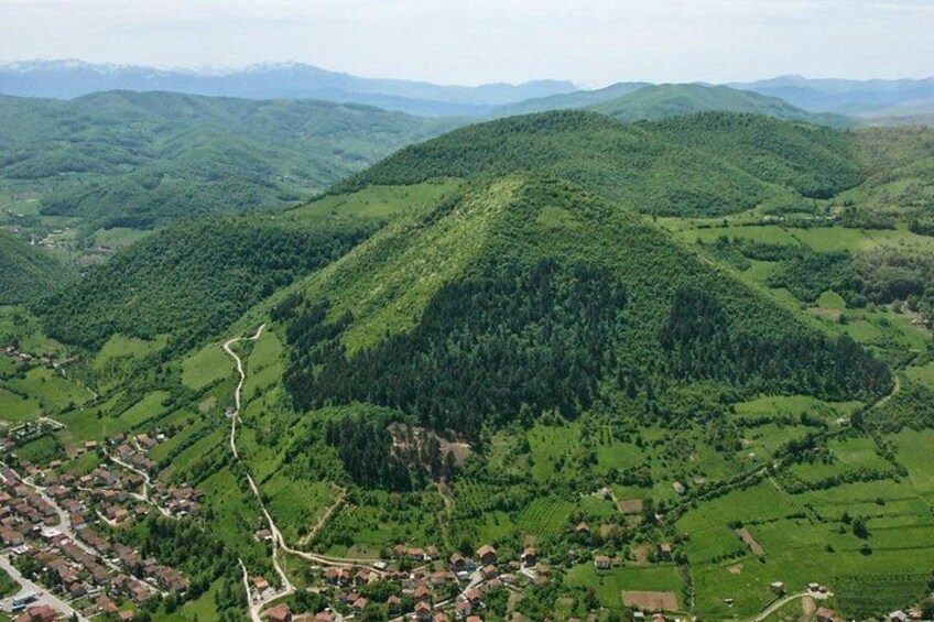 A mountainous landscape with a winding road, a small village, and dense forest areas. 1