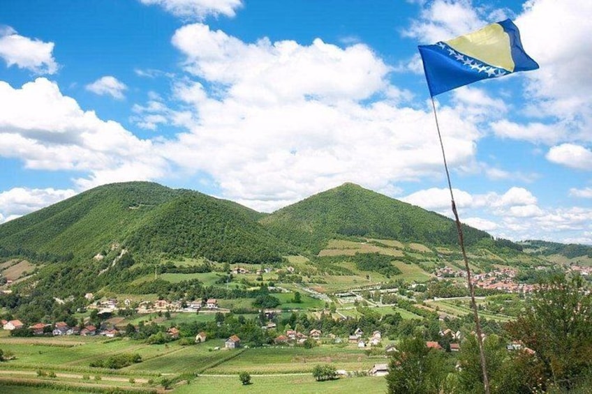 A mountainous landscape with a flag on a pole, a village in the valley, and a clear sky. 3