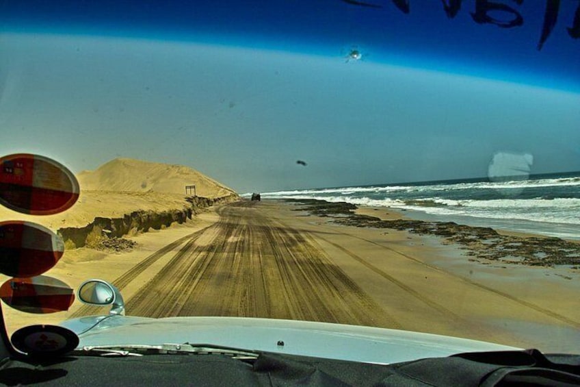 A beach with a dirt path leading to the ocean, a dune, and a vehicle parked on the sand. 2