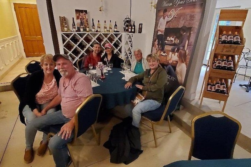 Un grupo de personas sentadas a una mesa en una tienda de vinos, con botellas exhibidas en estanterías al fondo. 2