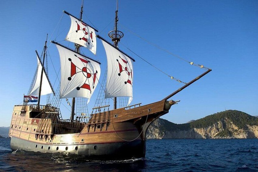 Un navire à voiles doté de plusieurs voiles, avec une coque en bois, et une côte montagneuse en arrière-plan. 2