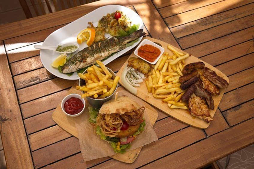 Une table en bois sur laquelle est servi un repas composé de poisson, de frites, d’un hamburger et d’une salade. 3