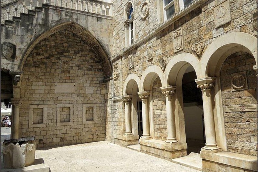 A stone building with an arched entrance, columns, and decorative shields. 5