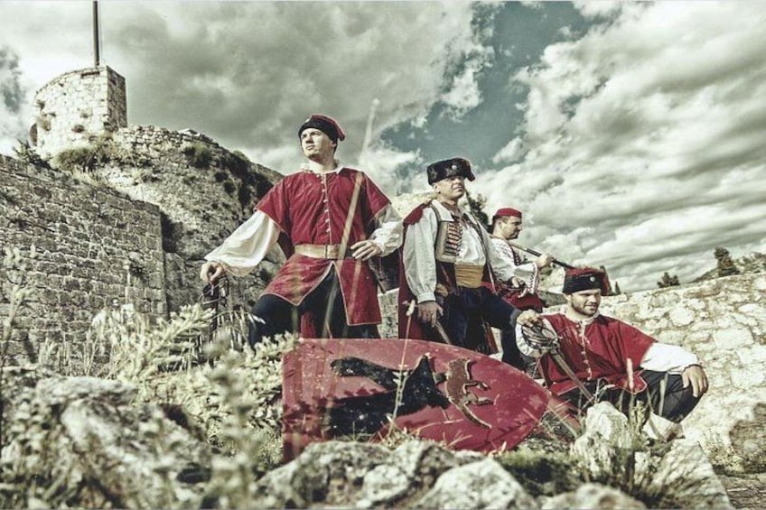 A historical reenactment scene with individuals in period costumes, a stone wall, and a cloudy sky. 4