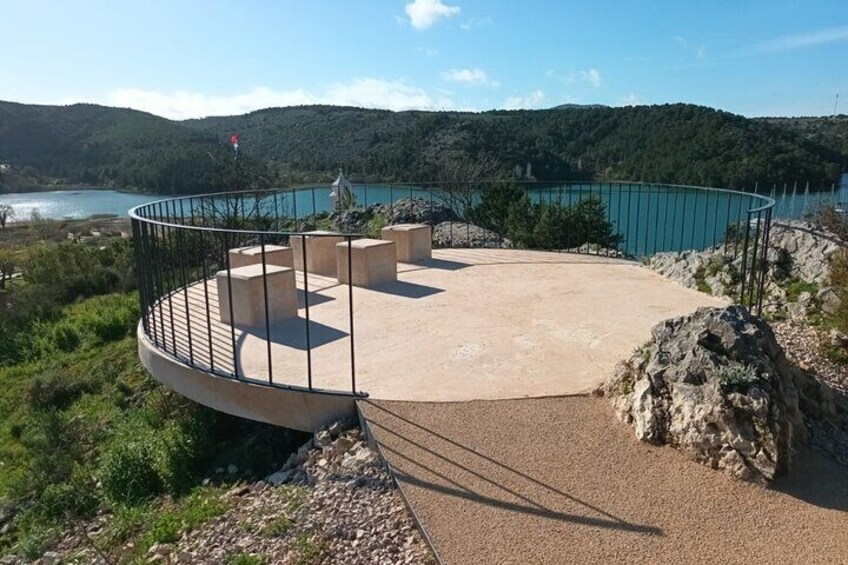 A circular viewing platform with a railing, overlooking a body of water and hills. 5