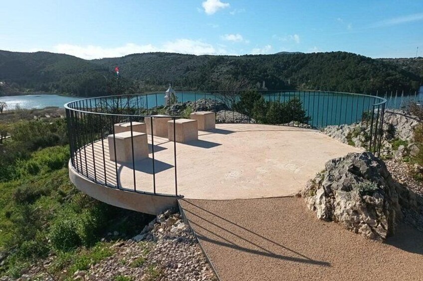 A circular viewing platform with a railing, overlooking a body of water and hills. 5