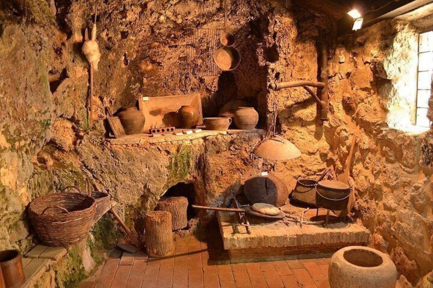 A rustic kitchen with stone walls, wooden utensils, and clay pots. 2
