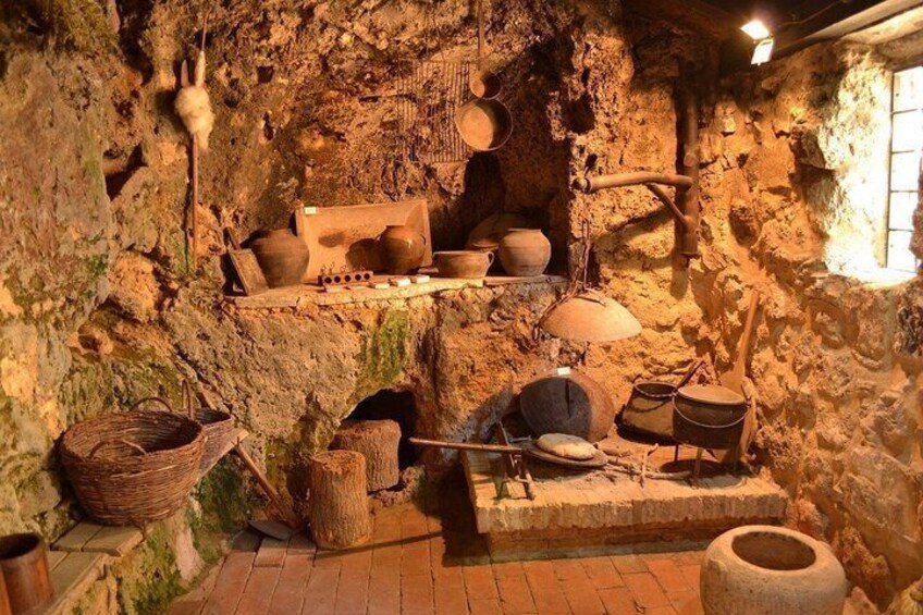A rustic kitchen with stone walls, wooden utensils, and clay pots. 2