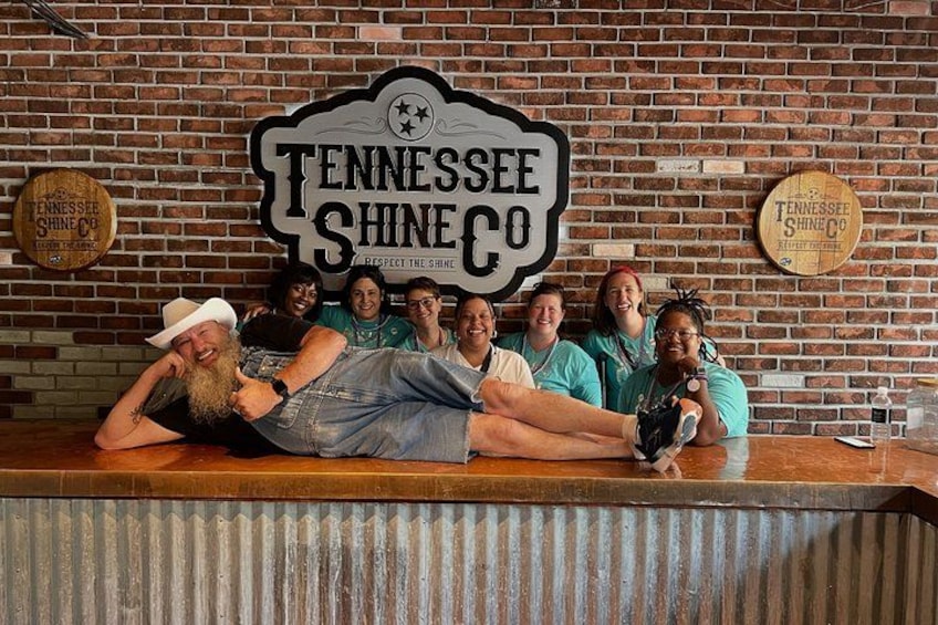 A group of people posing in front of a brick wall with a sign that reads 'Tennessee Shine Co.' 3
