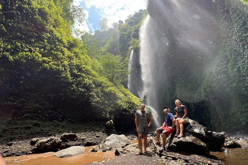 A waterfall, lush greenery, and people sitting on rocks. 1