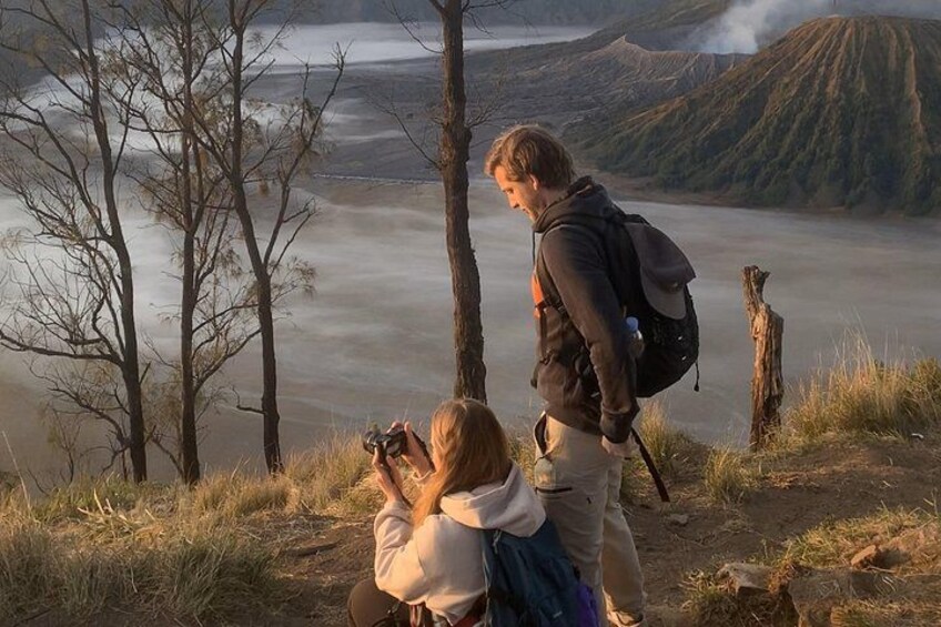 Two people taking photographs of a valley with a lake and mountains in the background. 2