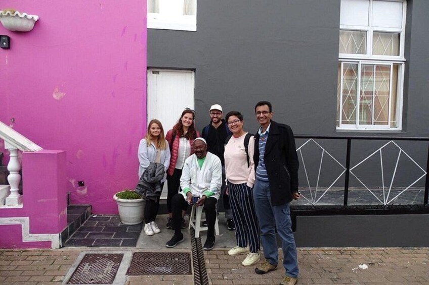 Een groep mensen staat voor een gebouw met een roze muur en een grijze deur. 1