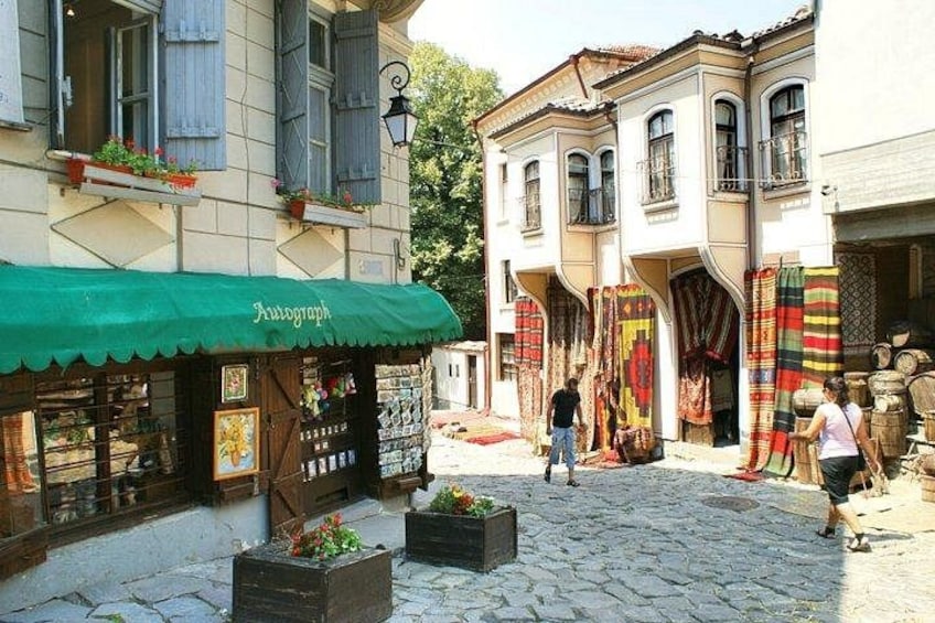 A cobblestone street with a shop displaying textiles and a green awning. 2