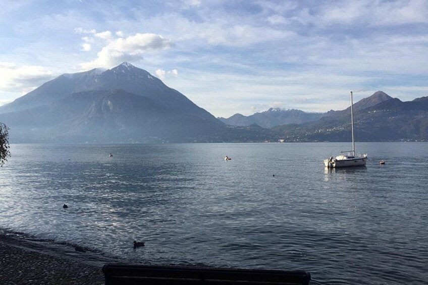 A calm lake with a sailboat anchored in the distance, surrounded by mountains and a clear sky. 4