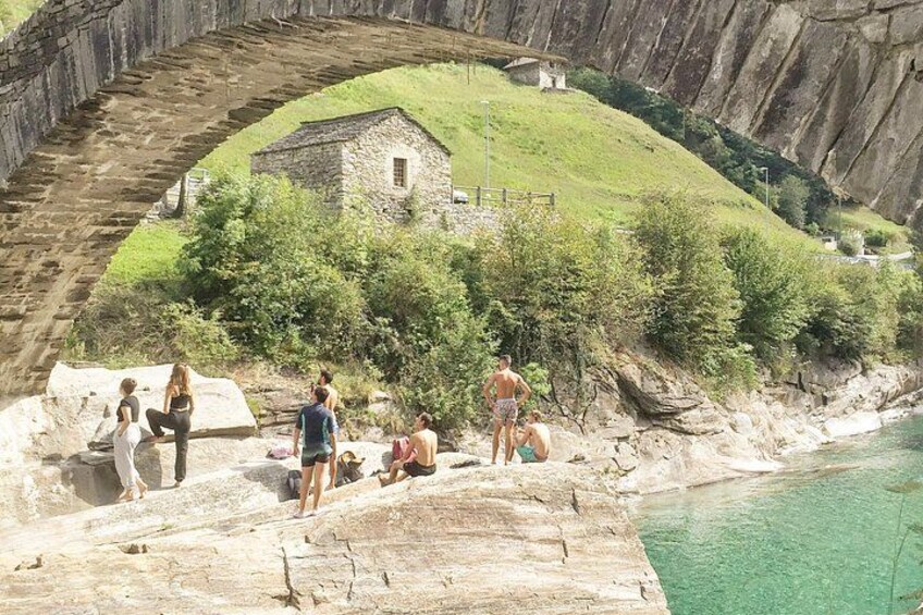A group of people on a rocky cliff overlooking a body of water, with a stone structure and greenery in the background. 3