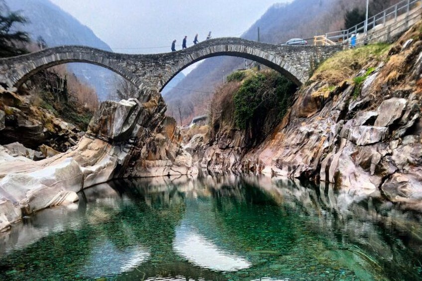 A stone bridge over a clear river, surrounded by rocky terrain and mountains. 2