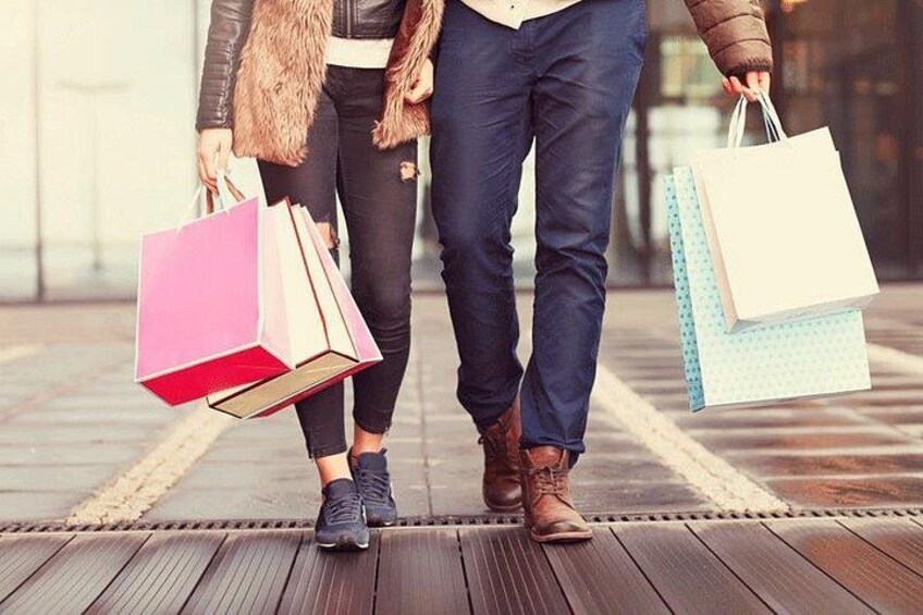 Two people walking on a wooden boardwalk, each carrying shopping bags. 3