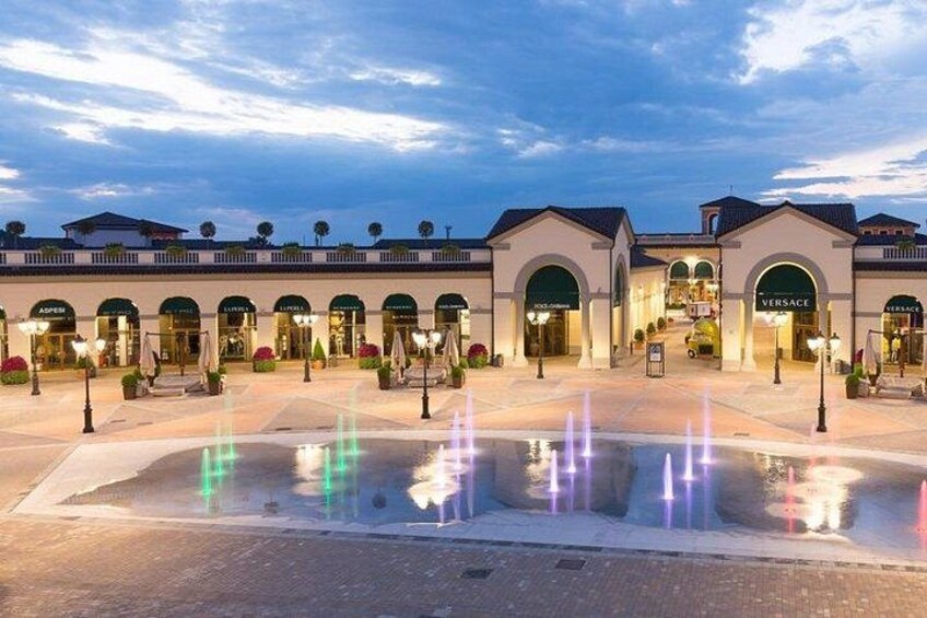 A shopping mall with multiple stores, including a Versace outlet, and a fountain in the center. 2