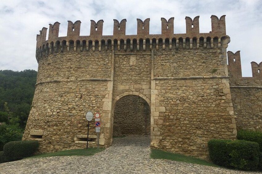 Eine historische Burg aus Stein mit einem großen Bogenportal, umgeben von Grünflächen und einem Kiesweg. 5