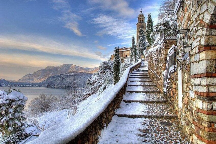 Una escalera de piedra cubierta de nieve que conduce a un edificio, con un lago y montañas al fondo. 2