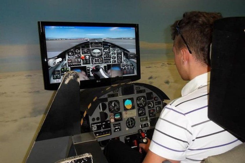 Una persona sentada dentro de un simulador de cabina con una pantalla mostrando una vista de vuelo. 4