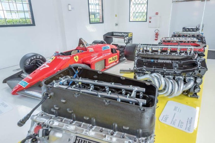 Un'auto da corsa rossa, un motore Ferrari e un tavolo giallo con documenti. 4