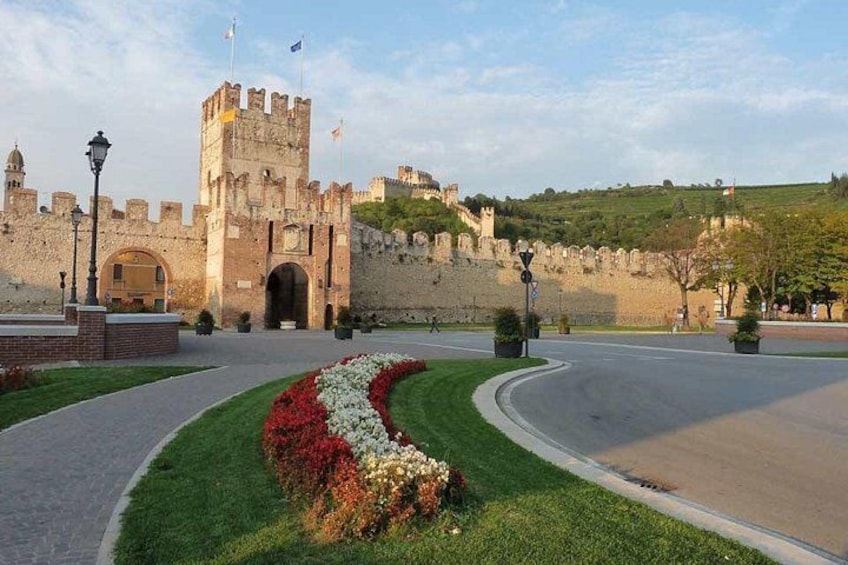 Un château historique doté d’une grande porte d’entrée, d’un jardin bien entretenu avec des fleurs aux couleurs vives et d’une route pavée menant au château. 4