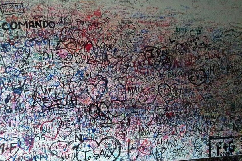 Een muur vol met verschillende teksten en tekeningen, waaronder namen en symbolen. 3