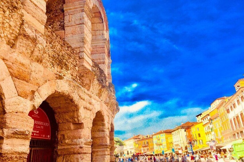 Une arche en pierre d’époque, surmontée d’une enseigne rouge, des bâtiments aux couleurs vives et un ciel d’un bleu éclatant. 1