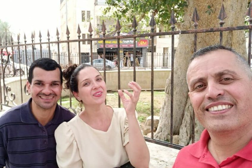 Three people sitting on a bench with a metal fence and trees in the background. 2